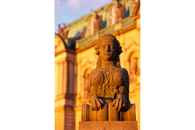 Statue of half woman, half lion with part of a building behind it