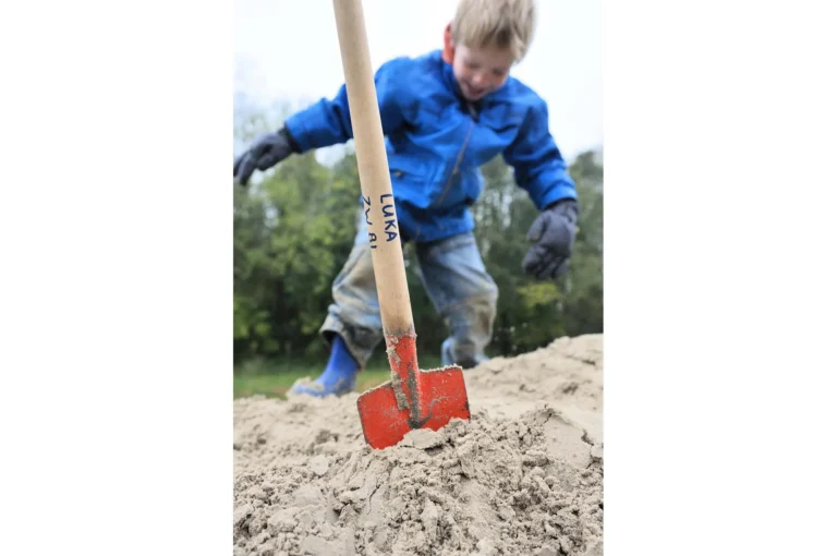 Jongen met schep spelend in zand