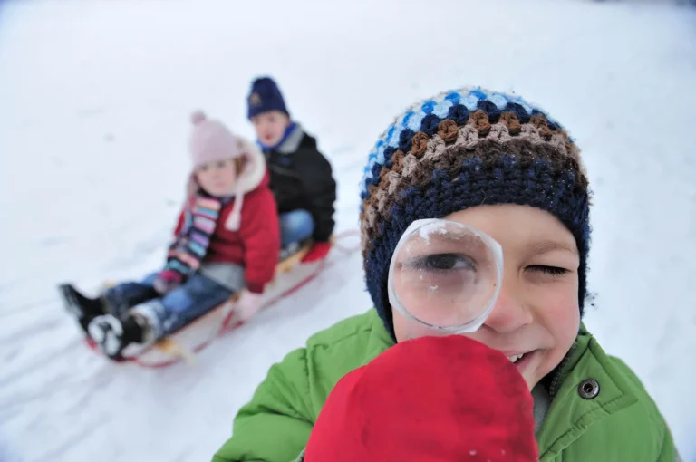 Kind kijkend door vergrootglas met twee kinderen op slee in achtergrond.