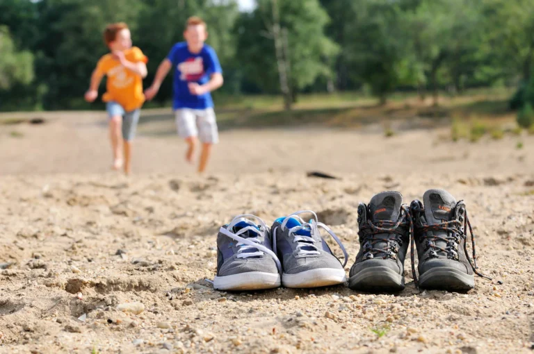 Rennende kinderen op stuifzand met schoenen in voorgrond.